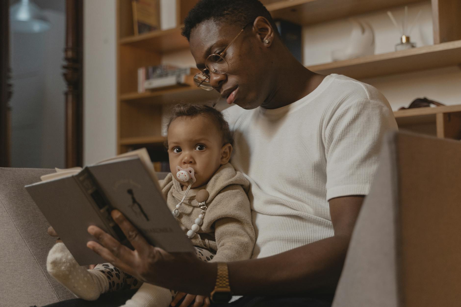 a man reading book to a baby with pacifier